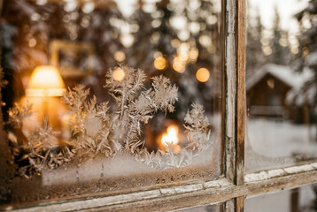 Macro view of frost ice crystals on wooden window glass with cozy warm cottage light in background