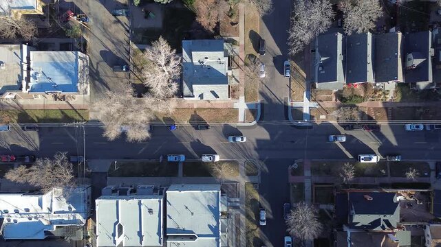 Top down descent shot view of residential blocks near Curtis Street form tight grid with pitched roofs, tree-lined sidewalks. Leafless canopy, varied roof textures waterscape, Denver, Colorado