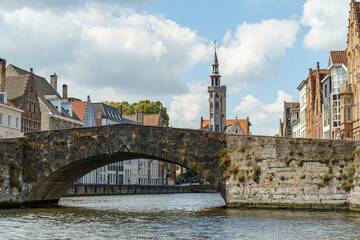Fototapeta premium A stone bridge over a canal in Bruges, Belgium. A tall Gothic church tower is visible in the background