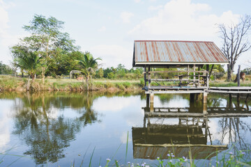 A wooden hut reflects in a calm pond under sunlight.