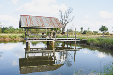 A wooden hut reflects in a calm pond under sunlight.