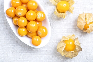 Goldenberries, Peruvian groundcherries, in a white bowl on linen. Ripe and fresh cape gooseberries, also called poha, Physalis peruviana, bright orange fruits, with papery lampion-like husks. Photo