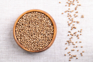 Coriander seeds, whole and dried, in a wooden bowl on linen. Fruits of Coriandrum sativum, a spice with lemony citrus flavor, due to the terpenes linalool and pinene, that enhances when roasted. Photo