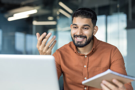 Man in brown shirt smiling and gesturing while participating in a virtual meeting or online conference from his office, actively communicating and collaborating