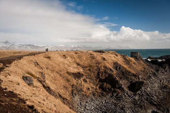 Northern destinations: Tourists on Hellnar-Arnarstapi coastal look-out enjoying breathtaking views of the ocean and snow-capped mountains, Snaefellsnes peninsula (region of Vesturland, Iceland)