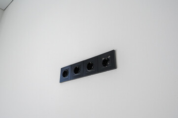 Obraz premium row of four sleek black electrical outlets mounted on a clean white wall, minimalist design, modern look, uniform alignment, contemporary interior detail.