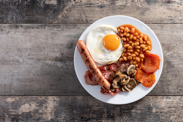 Full English breakfast with fried egg, bacon, sausages and beans on wooden table. Top view. Copy space