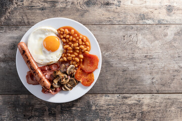 Full English breakfast with fried egg, bacon, sausages and beans on wooden table. Top view. Copy space