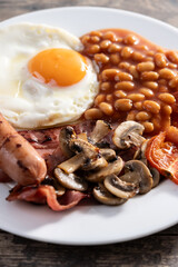 Full English breakfast with fried egg, bacon, sausages and beans on wooden table