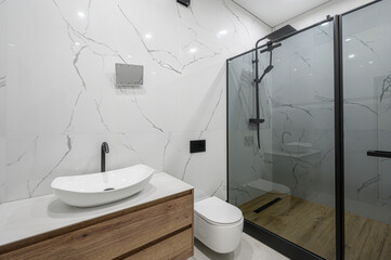 Modern minimalist bathroom with white marble walls, glass shower enclosure, wooden vanity, oval...