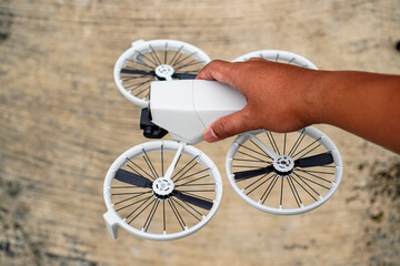 A hand holds a white quadcopter drone with four propellers against a textured wooden background...