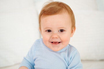 Baby close-up portrait, smiling and joyful little child on a white bed in a blue bodysuit