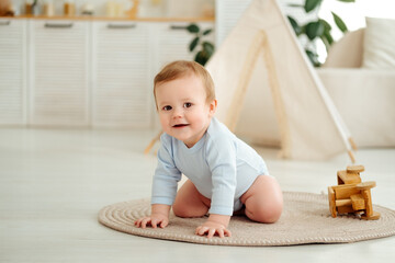 A smiling and joyful kid is crawling on the floor near the wigwam in the children's room at home, a small child is learning to crawl in a blue bodysuit and laughing © Any Grant