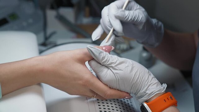 Removing excess gel from nail edges with orange stick and gloved hands during final coating stage
