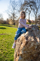 Little girl jumping on decorative stones in city park. Active spring play and outdoor childhood lifestyle.