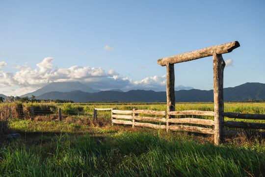 Rural landscape, farmland, featuring a wooden fence and gate with mountains in the background. On the road in between Daintree and Mossman, where the Daintree Rainforest meets the Great Barrier Reef i