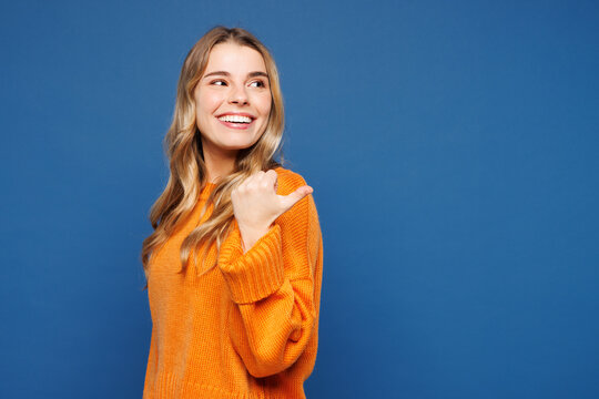 Side view young happy smiling cheerful woman wear yellow sweater casual clothes point thumb finger aside indicate on area mockup isolated on plain blue background studio portrait. Lifestyle concept.
