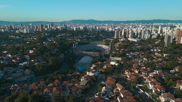 Aerial tilt-up of Pacaembu Stadium. The iconic soccer field, athletic complex, and the dense residential and high-rise skyline of S&atilde;o Paulo at dawn.