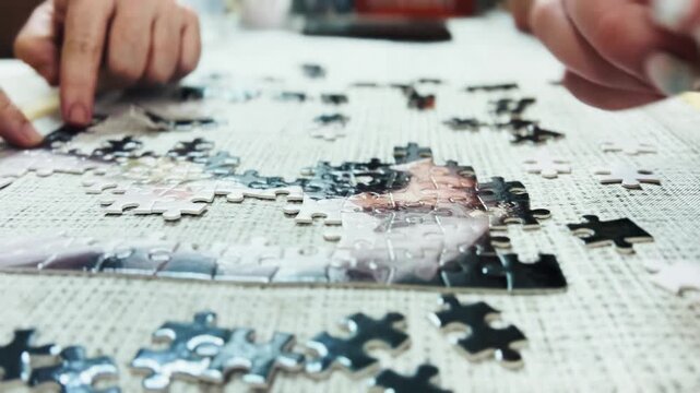 Close-up of multiple hands collaborating to assemble a jigsaw puzzle on a table. Cooperative leisure activity requiring focus and patience.