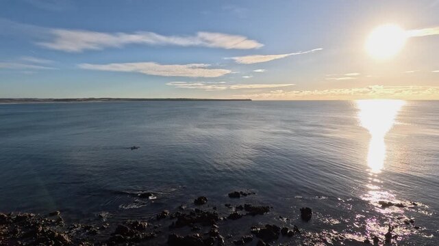 Small distant sea kayakers on calm ocean near rocky shore, afternoon