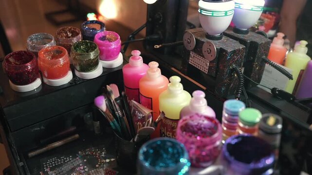 Glitter party makeup station at a birthday event displays colorful pigments, shimmer powders, brushes, and cosmetic bottles arranged for creative face art, festive beauty styling, dolly in shot