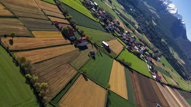 Aerial view of lush, patchwork farmland with snow-capped mountains. Captured at a tilted angle, perfect for a scenic video backdrop.