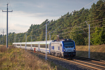 Obraz premium Szybka nowoczesna lokomotywa z wagonami pędzi po torach