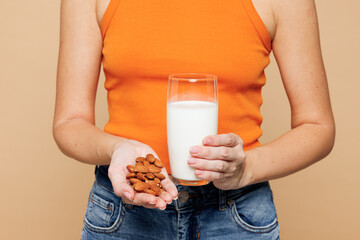 Cropped close up young woman wear orange top casual clothes drink almond milk hold nuts in palm...