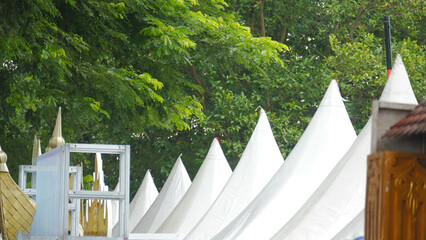 Row of White Conical Event Tents Under Green Trees Against Bright Sky