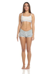 Fototapeta premium Studio shot of a woman with dark hair wearing a white sports top and gray shorts, standing barefoot in front view, full body, on a white background