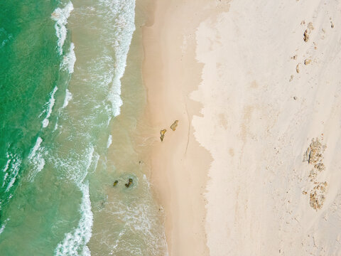 Aerial view of the sandy beach kissed by the turquoise sea, where the waves curl gently towards the shore creating a beautiful contrast of colors, Betty's Bay, Western Cape, South Africa.