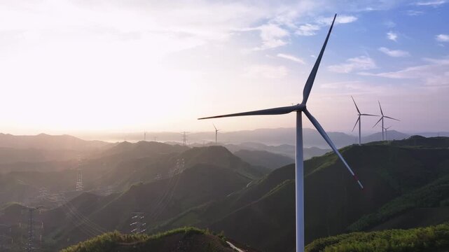 Wind turbines standing on mountainous terrain during sunrise with golden light and clear sky