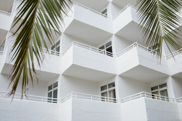 White minimalistic hotel building exterior with symmetrical balconies on Mallorca island in Spain. Leaves of palm tree growing near