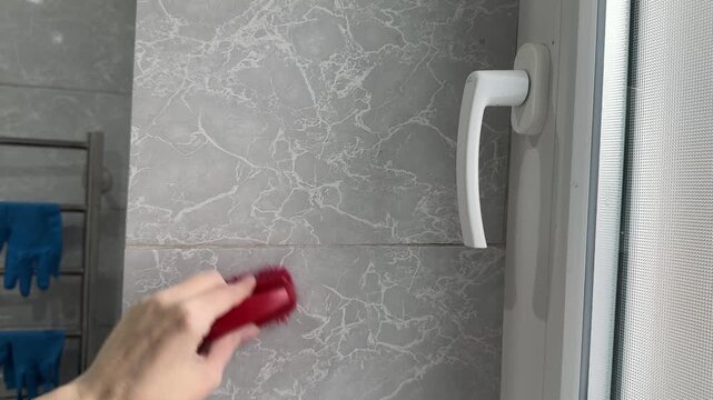 Female hands scrub bathroom tile grout lines with cleaning brush closeup