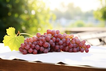 Naklejka premium Fresh red grapes and a bright green leaf resting on a white surface outdoors