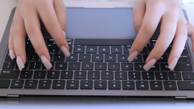 Woman is typing on a laptop keyboard. She is using her fingernails to type. The keyboard has a number pad and a space bar