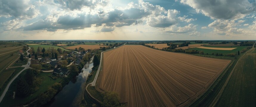 Panoramic drone image of a Moldovan village close to a river featuring hills, farmland, clouds, and godrays