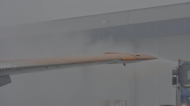 Snow removal vehicle sprays orange de-icing fluid onto aircraft wing, showcasing efficient winter maintenance process in action, ensuring safe flight operations during harsh weather conditions