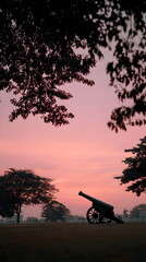 Historic cannon silhouette against vibrant sunset sky and trees  