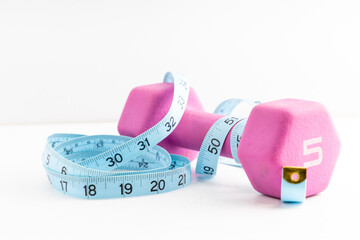 Pink dumbbell and measuring tape on a white background, symbolizing fitness and weight loss goals
