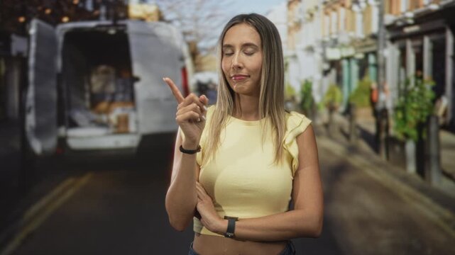 Woman points index finger upward on street beside an open van filled with packages, arms crossed at waist and subtle smile visible; calm reflection.