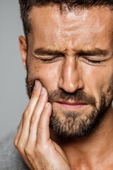 Obraz premium Young man shows pain from dental issue while touching his face against gray background