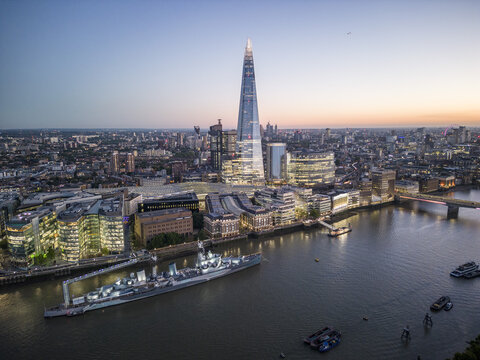 Aerial view of The Shard piercing the skyline, casting a long shadow over the Thames, its glass facade reflecting the soft glow of twilight, London Bridge, London, United Kingdom.