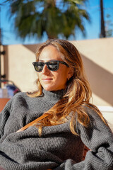 A woman wearing sunglasses and a black sweater sits on a chair