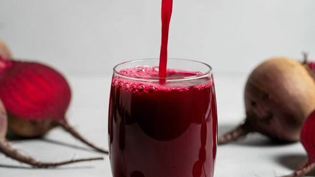 Pouring fresh beetroot juice into a glass, surrounded by whole and sliced beets.