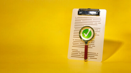 Magnifying glass on checklist clipboard with green check mark for verification and approval concept.