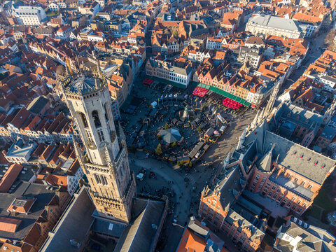Aerial view of the Markt square bustling with activity, the iconic Belfry tower casting long shadows over the colorful market stalls, Bruges, Flanders, Belgium.