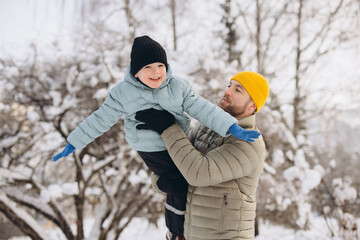 Father and son playing in winter park, dad lifting child in air, enjoying family moments outdoors in nature