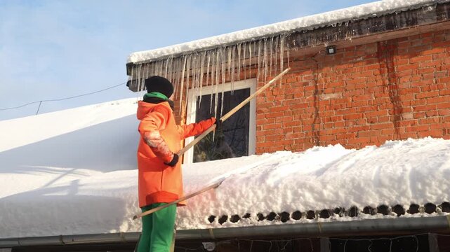 Slow motion camera shot of Caucasian woman knocking down the icicles from the gutter. Female working outside during cold winter. Snowstorm.