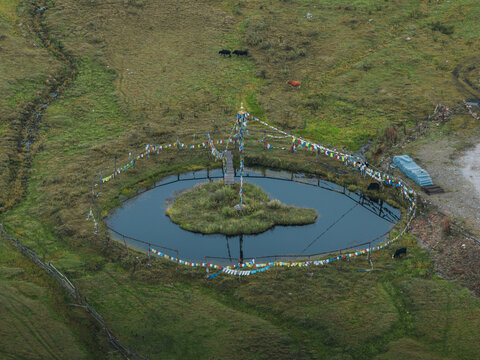 Aerial view of the serene pond with a small island at its center, adorned with colorful prayer flags fluttering gently in the breeze, Phobjikha Valley, Wangdue Phodrang, Bhutan.